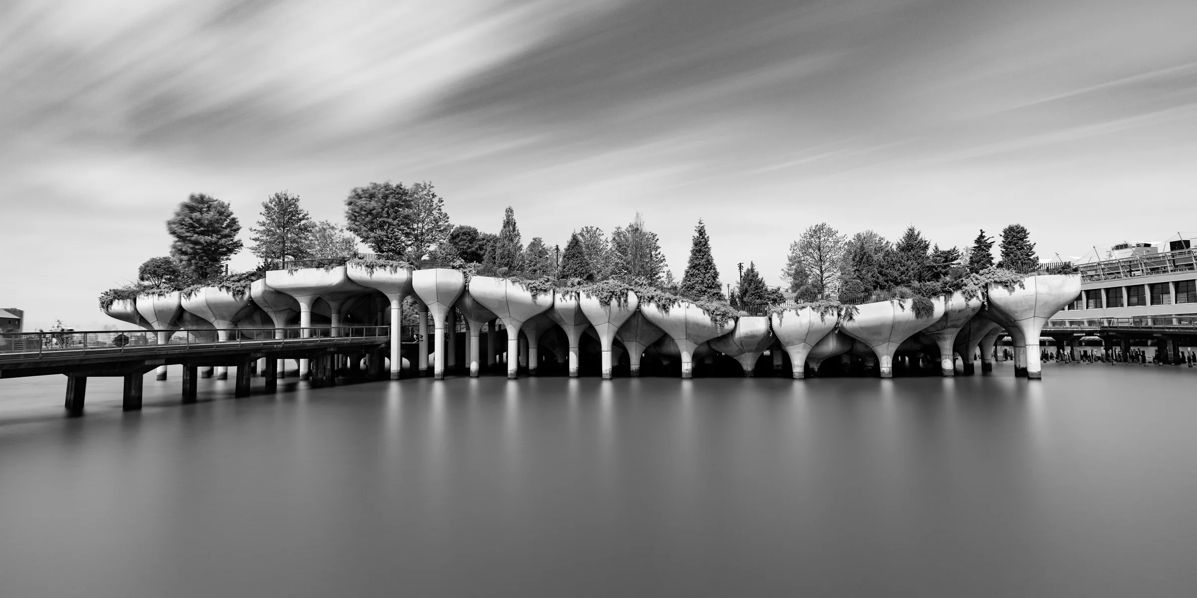 Long exposure black-and-white photograph of a building with tulip-shaped concrete piers over water, by ARCHTRAITS