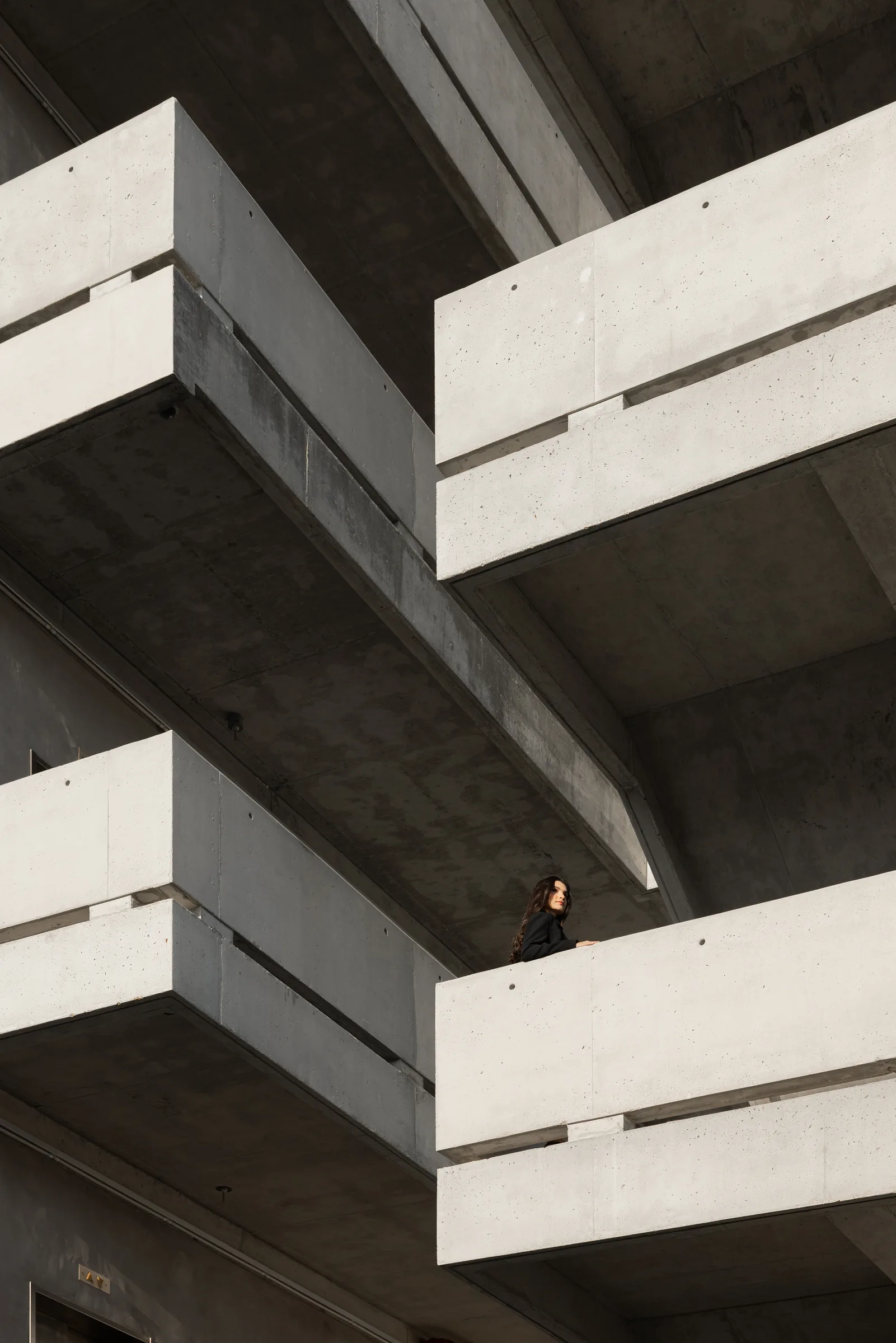 Dramatic concrete cantilevered balconies with a woman standing on the lower balcony, architecture photography by ARCHTRAITS